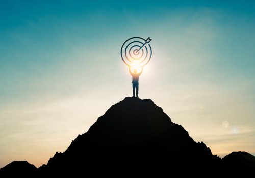 Silhouette of businessman holding target board on the top of mountain with over blue sky and sunlight. It is symbol of leadership successful achievement with goal and objective target.